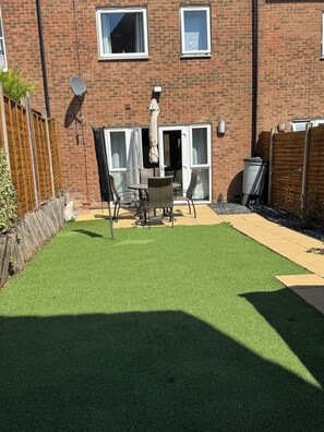 A backyard with artificial grass, a patio table, chairs, and a wooden fence. - Modern 3Bedroom House, Garden, Free Parking, Sleeps 7, Easy Central London Reach (Orpington)