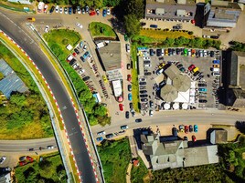 Vista aérea de un estacionamiento con múltiples filas de coches, una glorieta y edificios circundantes.