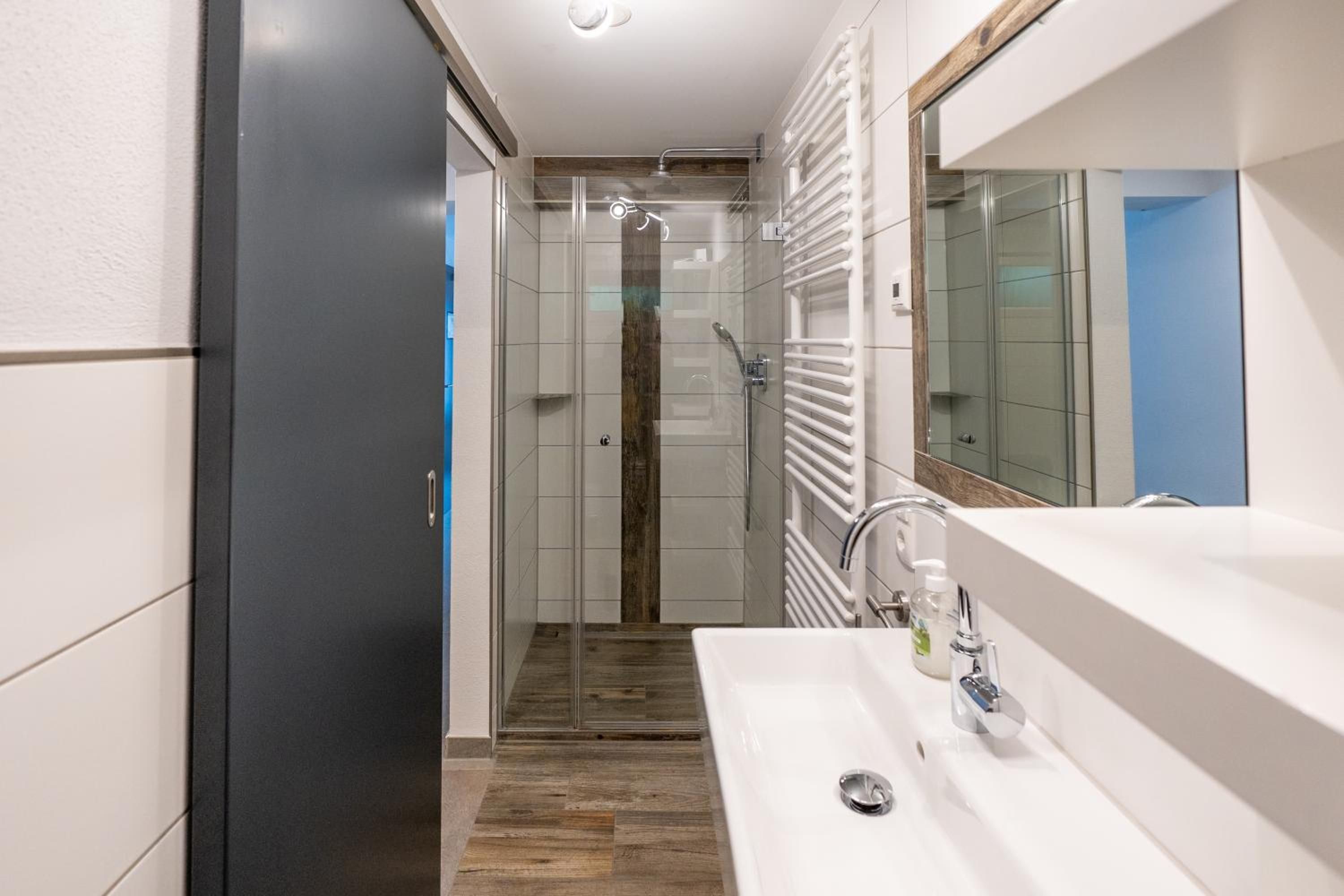 Een moderne badkamer met een douche, wastafel en spiegel.