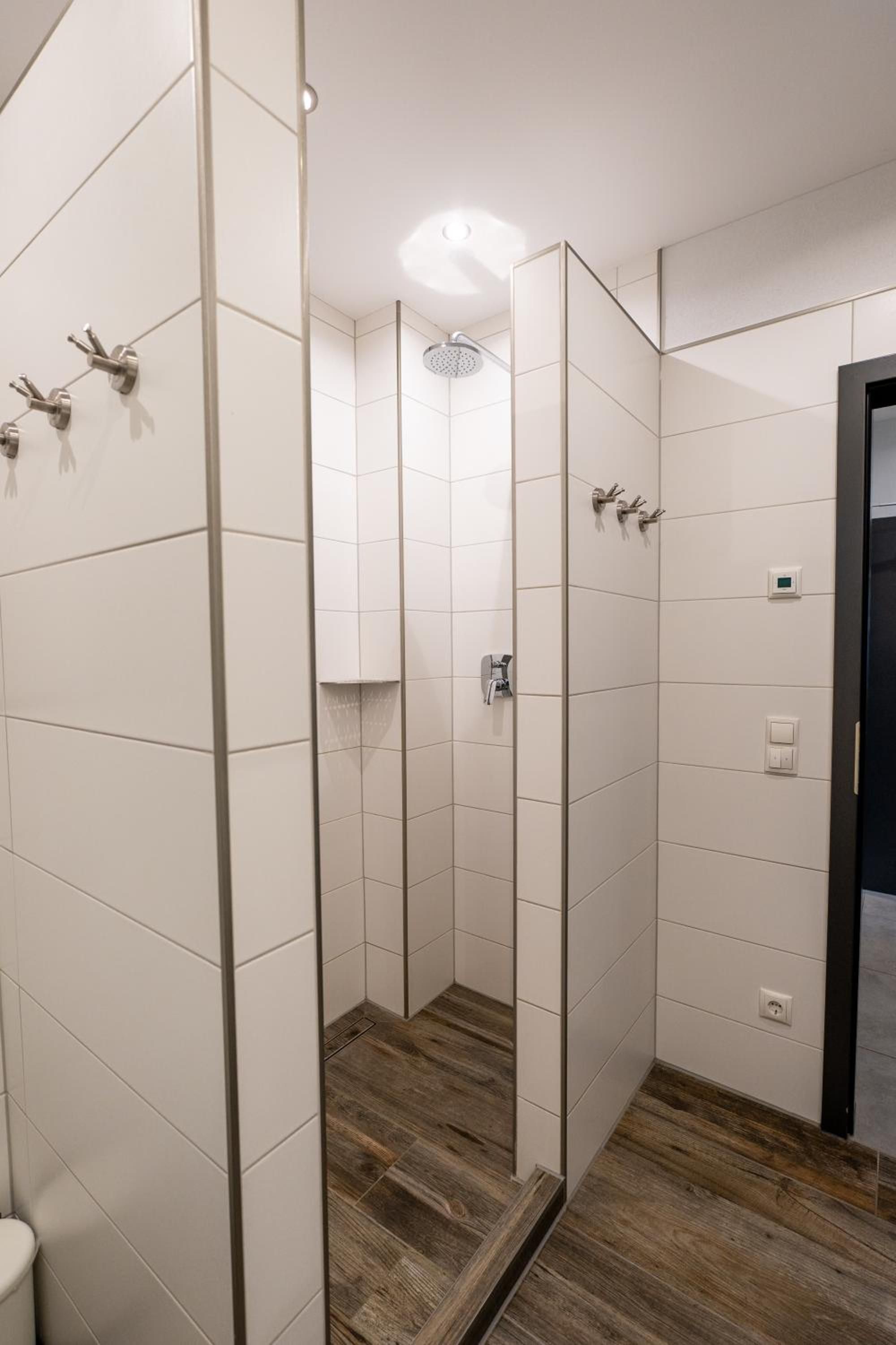 Ein modernes Badezimmer mit weißen Fliesen, einer Dusche mit Glastür und Holzboden.