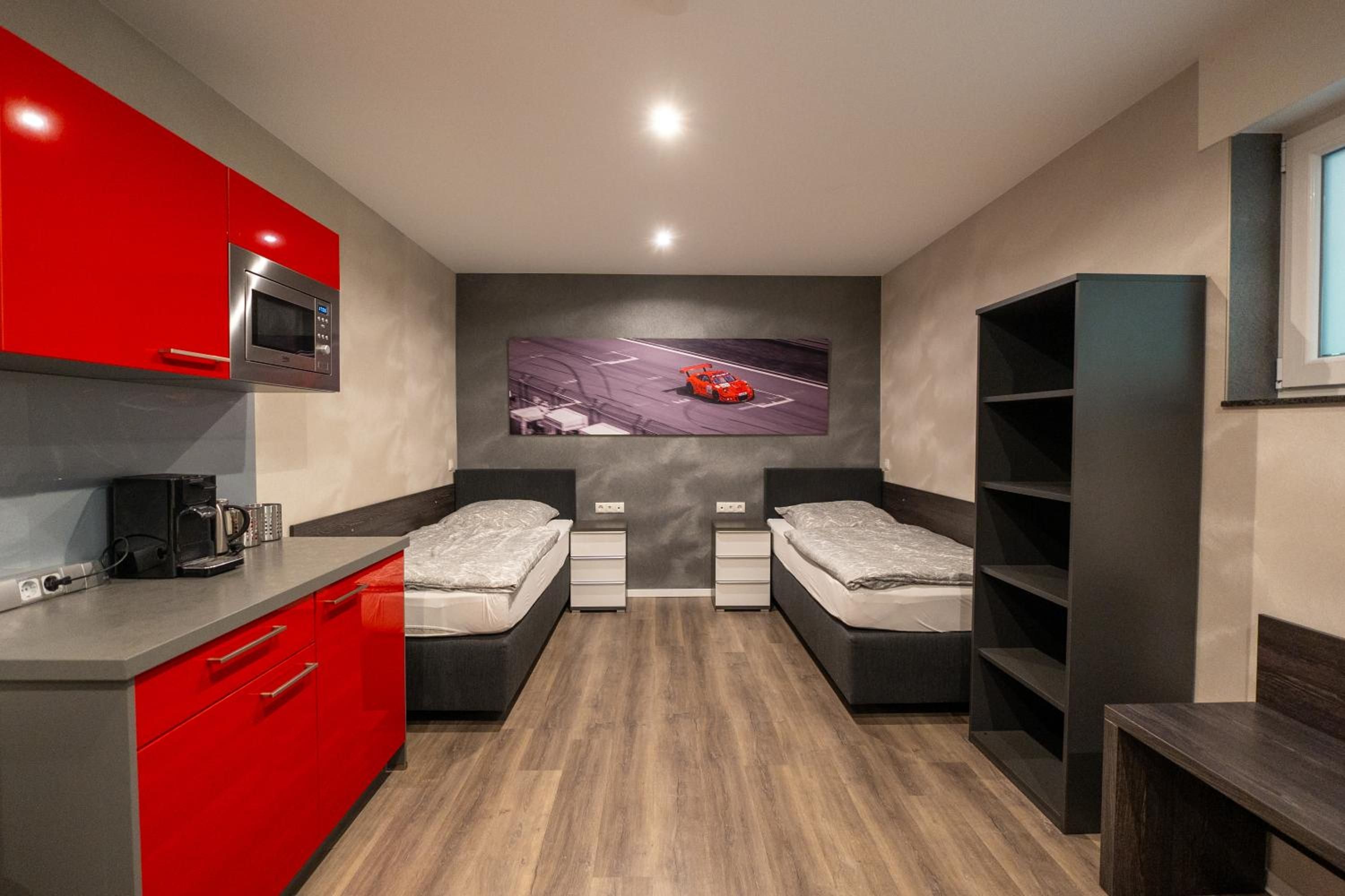 Een kleine kamer met kitchenette, twee bedden, een aan de muur bevestigde televisie en een raam.