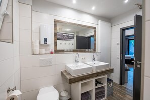 A modern bathroom with two sinks, a toilet, and a mirror. - Guesthouse Cockpit (Adenau)
