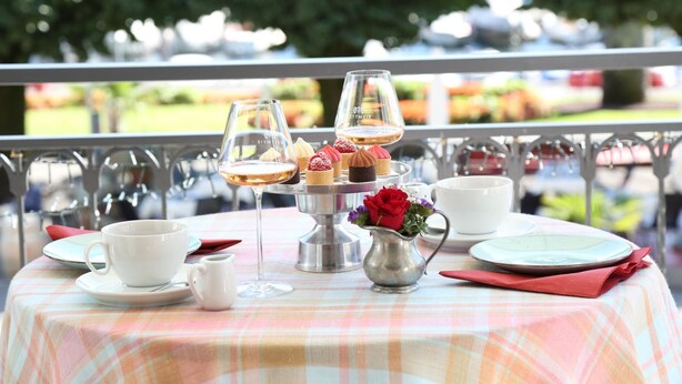 Una mesa lista para una comida, con mantel a cuadros, un jarrón de flores y un pastelero de varios niveles.