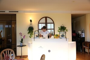 A person standing behind a reception desk in a room with a large arched window, a small table with a potted plant, and a chair. - Al Pozz Boutique Resort (Muralto)