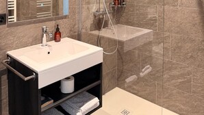 Un baño moderno con ducha de vidrio, un lavabo blanco y un espejo encima.