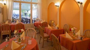 Un restaurante con mesas redondas, sillas y vistas a la calle a través de amplios ventanales.