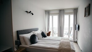 Un dormitorio con cama, mesita de noche, lámpara y vistas al exterior por la ventana.