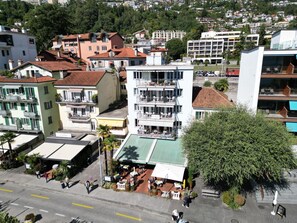 Un edificio de varios pisos con un restaurante en la planta baja, rodeado de otros edificios y vegetación.