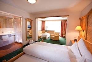 A hotel room with a bed, a sitting area with a table and chairs, a television, and a bathroom with a mirror and sink.