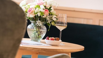 A table with a vase of flowers, a glass of white wine, and a bowl of assorted pastries.
