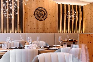 A restaurant interior with wooden panel walls, a central clock, and geometric light fixtures.