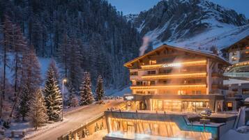 A multi-story hotel with a pool area, surrounded by snow-covered trees and mountains.