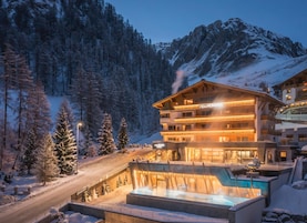 Un hotel de varios pisos con zona de piscina, rodeado de árboles nevados y montañas.