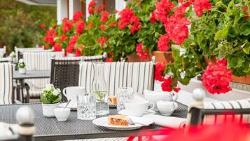 An outdoor seating area with tables, chairs, and a variety of plants.