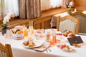 A breakfast setting with various food items, a teapot, a pitcher of orange juice, and a candle on the table.