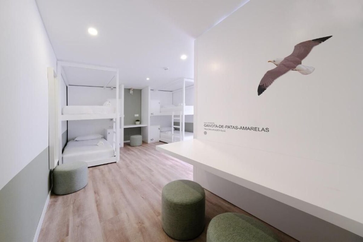 Quarto moderno e minimalista com beliches, parede branca com ilustração de gaivota e um pequeno banquinho verde.
