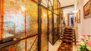 Un pasillo con una escalera, un separador de vidrio con diseños coloridos y un arreglo floral.