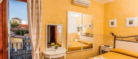 A hotel room with a bed, a bedside table, a mirror, an air conditioning unit, and a view of the outside.