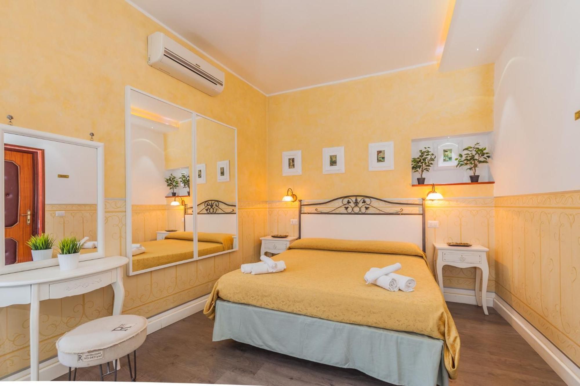 A hotel room with a bed, bedside tables, a mirror, a dresser, and a small stool.