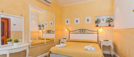 A hotel room with a bed, bedside tables, a mirror, a dresser, and a small stool.