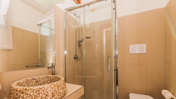 Un baño con ducha de vidrio, lavamanos con diseño de guijarros y un inodoro con un rollo de papel higiénico.