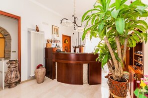 Una zona de recepción con mostrador de madera, una planta en maceta, un teléfono antiguo y un aplique de pared.