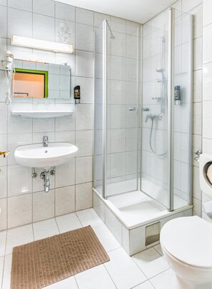 Ett modernt badrum med en dusch som är avskärmad med glasväggar, ett handfat och en toalett.