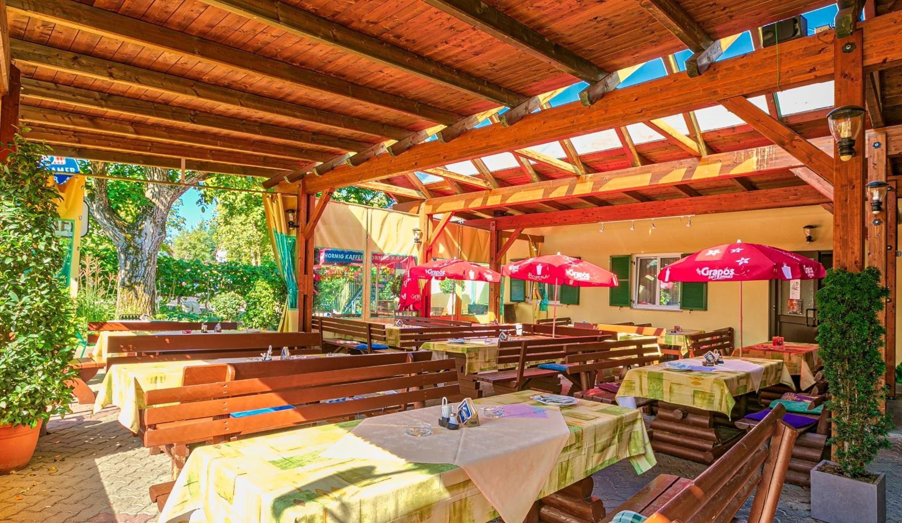 Un espace de restauration en plein air, doté de tables et de bancs en bois, et surmonté d’une structure de toit en bois.
