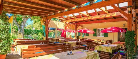 Un espace de restauration en plein air, doté de tables et de bancs en bois, et surmonté d’une structure de toit en bois.