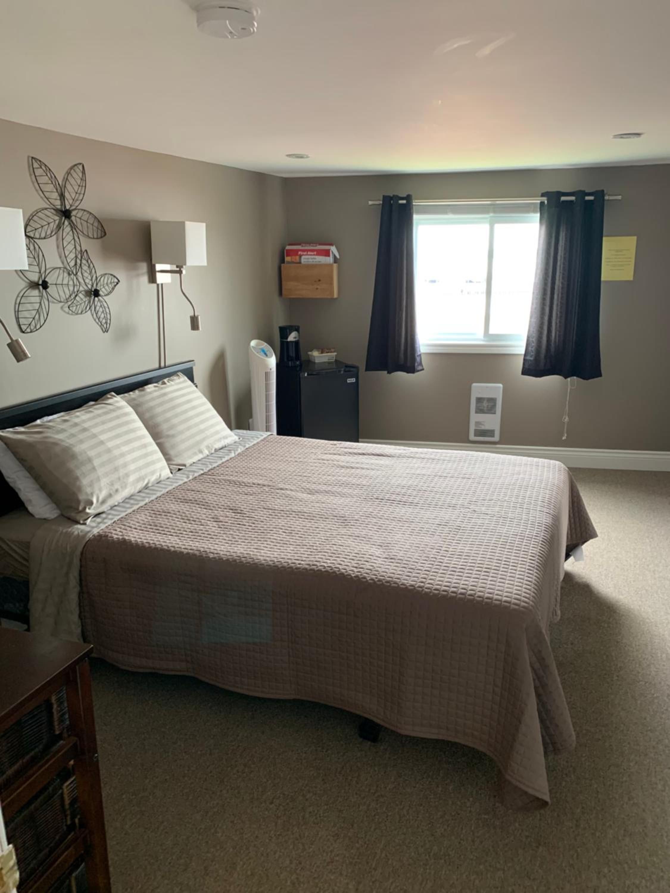 A bedroom with a bed, bedside lamps, a heater, a window with curtains, and a wall decoration.