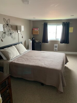 A bedroom with a bed, bedside lamps, a heater, a window with curtains, and a wall decoration.