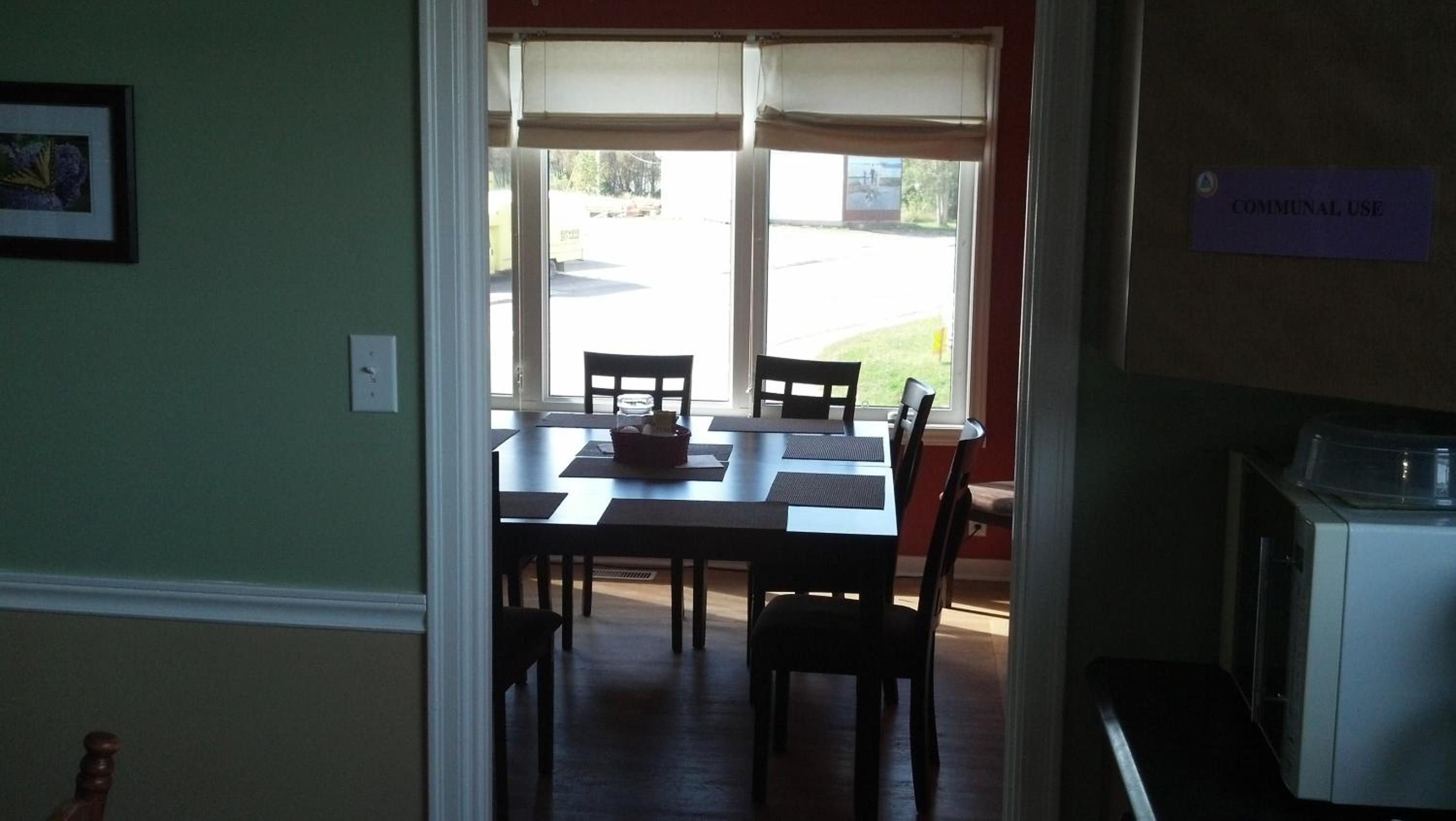 A room with a dining table and chairs, a window with a view of the outside, and a sign indicating 'COMMUNAL USE'.