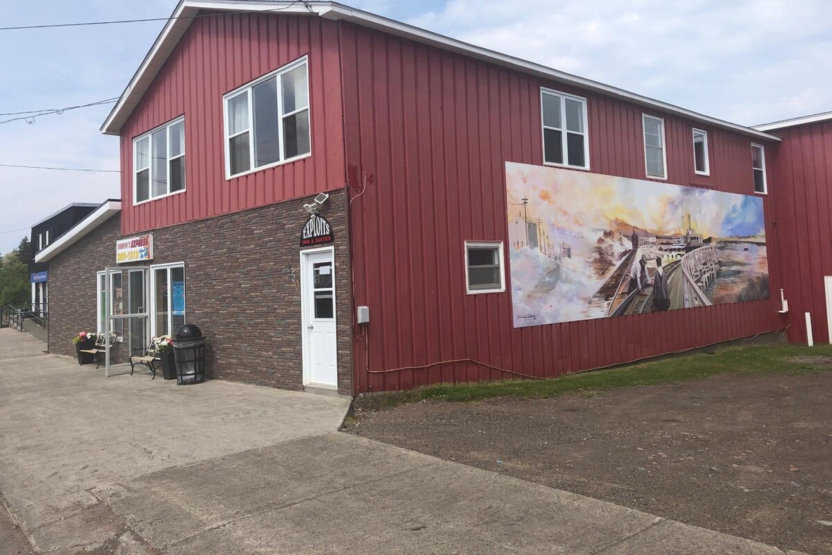 A red building with a large mural on the side, a sign for a business, and a door.
