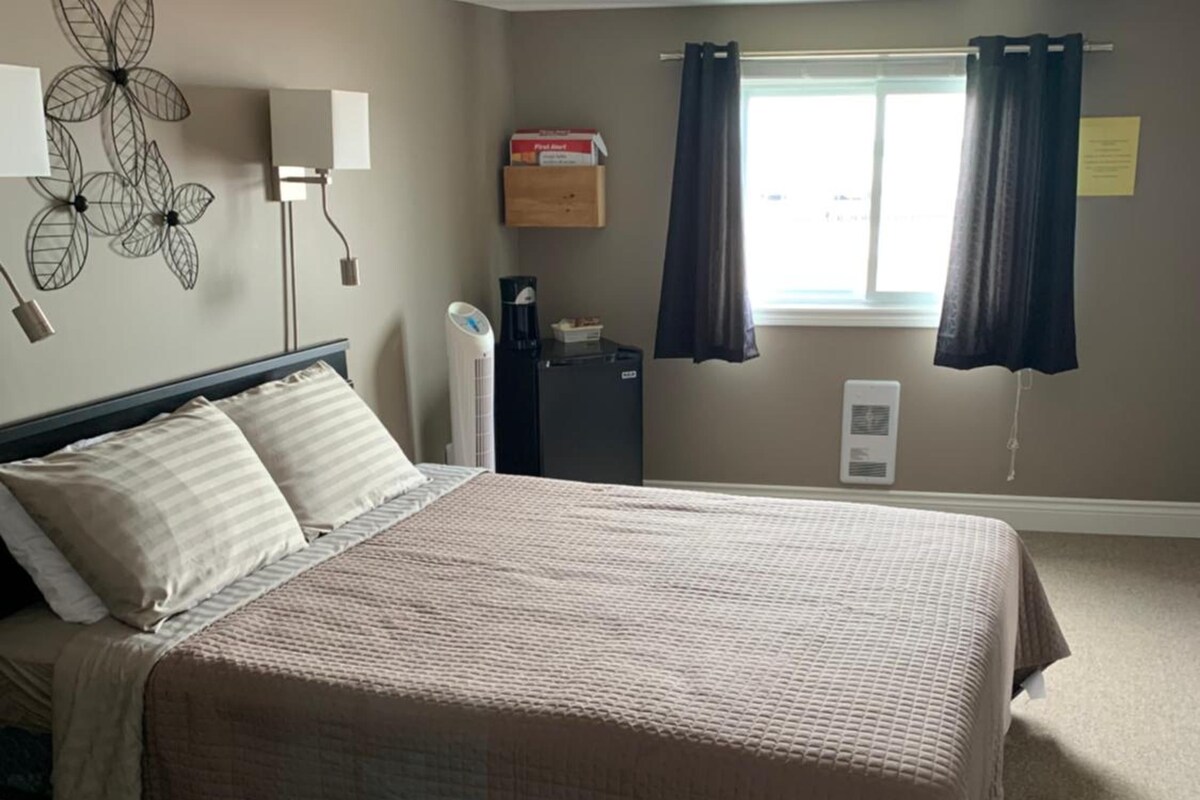 A bedroom with a bed, bedside lamps, a heater, a window with curtains, and a wall decoration.