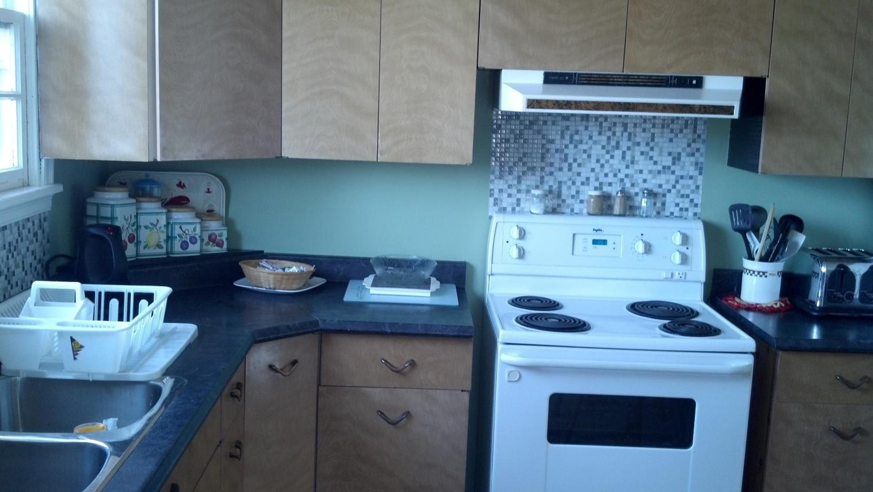 A kitchen with a white stove, wooden cabinets, a tiled backsplash, and a window.