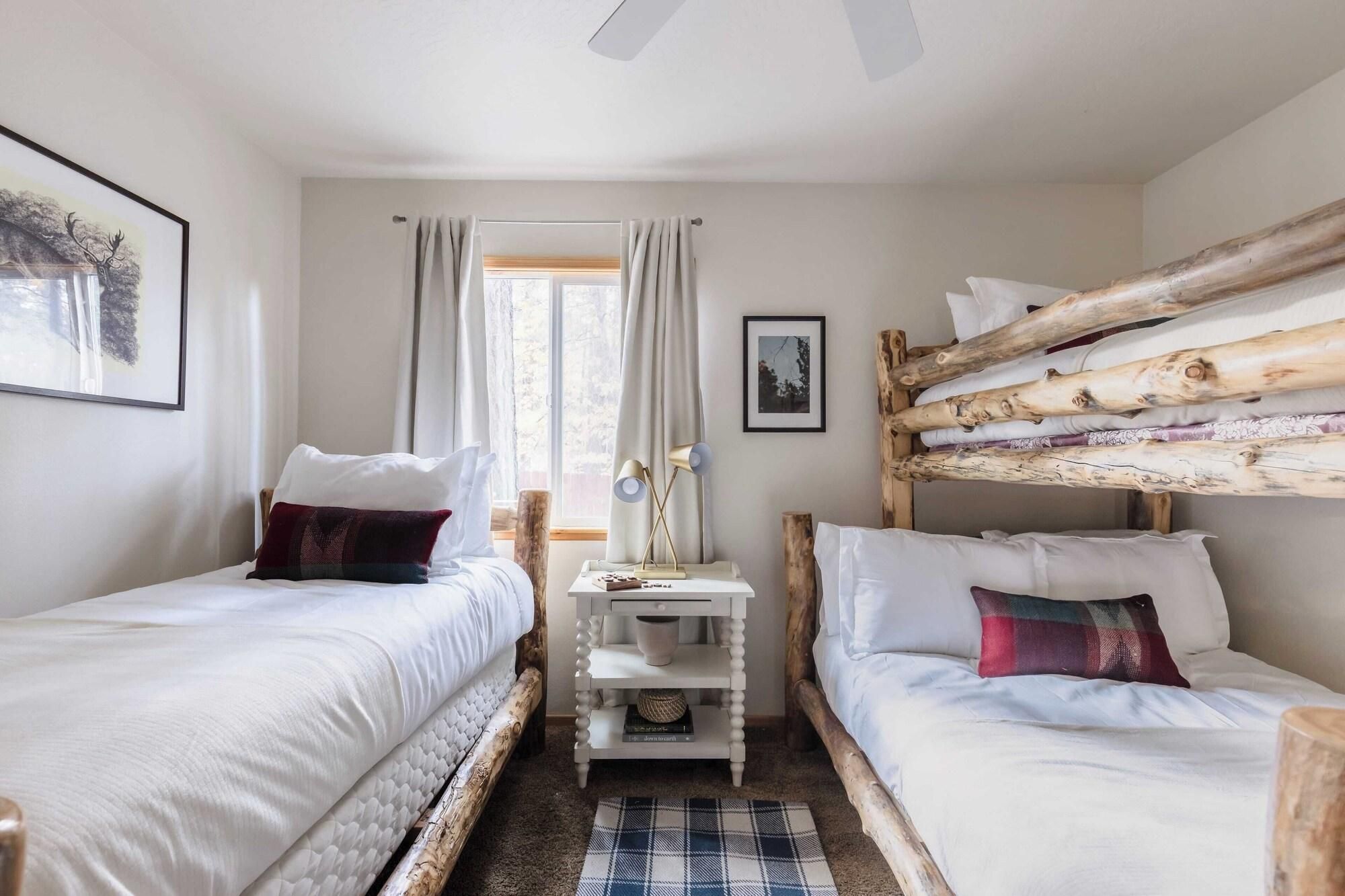 Quarto com duas camas, uma mesinha e janela com cortinas.