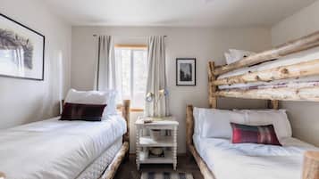 Quarto com duas camas, uma mesinha e janela com cortinas.