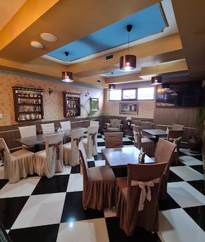 Un restaurante con piso a cuadros, mesas con sillas, lámparas colgantes y una zona de bar con estanterías.