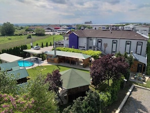 A residential property with a swimming pool, a covered outdoor seating area, and a large building with a distinctive purple and white facade.