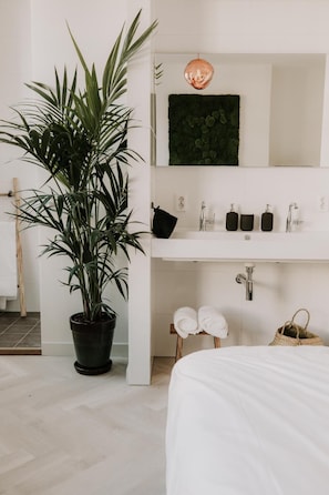 Een badkamer met een wit wastafelmeubel, een spiegel, een potplant en een handdoekrek.
