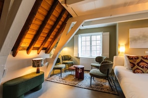 Een gezellig loft slaapkamer met schuine wanden, een groot raam en een combinatie van zitplaatsen, zoals een bank en stoelen.
