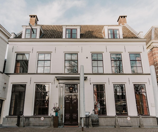Een gebouw met twee verdiepingen, een symmetrische gevel, grote ramen en een centrale ingang met een deur.
