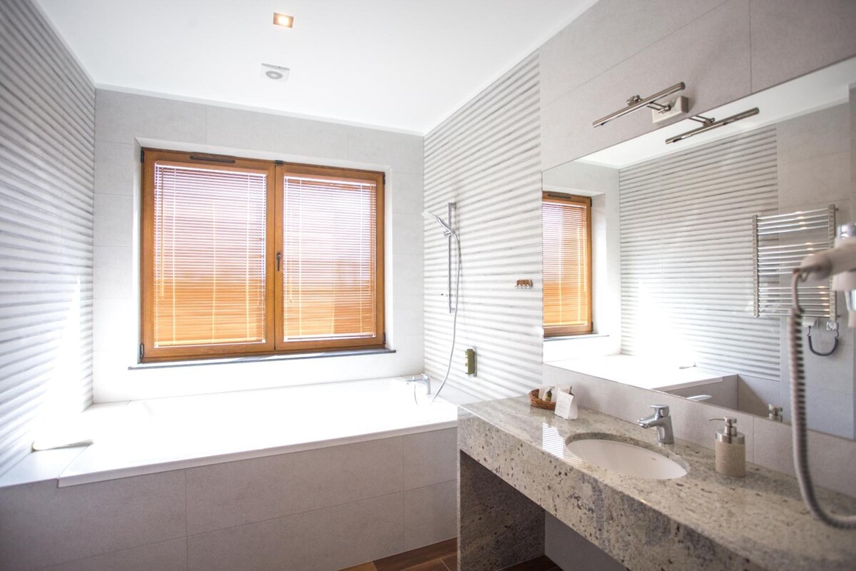 A modern bathroom with a large window, a bathtub, a sink, and a shower.