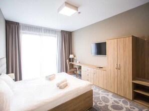 A hotel room with a large bed, a desk, a chair, a TV, and a wardrobe. - Hotel Rondo (Wabrzezno)