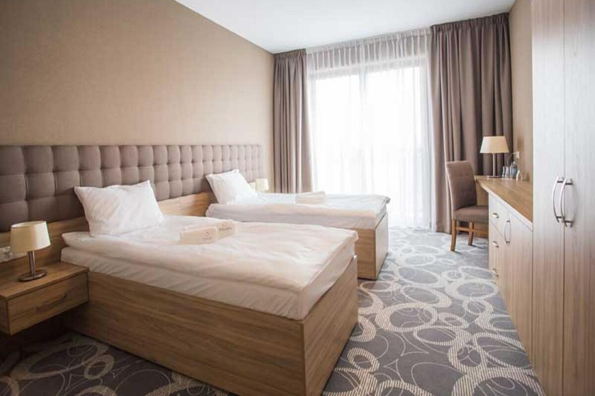 A hotel room with two beds, a desk, a chair, and a wardrobe.