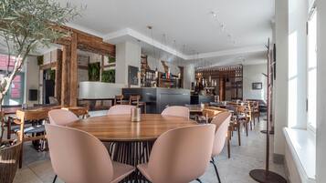 Un comedor moderno con una mesa de madera central rodeada de sillas, una cocina al fondo y un ventanal que proporciona luz natural.
