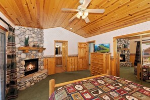 A cozy room with a stone fireplace, wooden ceiling, and a quilted bedspread. - Teakwood Cozy Wood Cabin With Fireplace (Big Bear Lake)