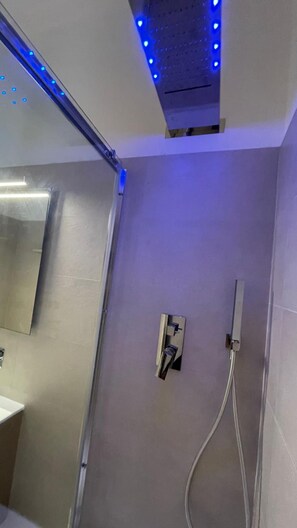A bathroom with a shower, a mirror, and a light fixture. - Hotel Boschetto (Follonica)