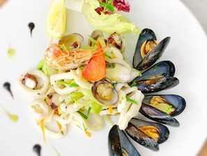 A seafood salad with mussels, clams, and shrimp, garnished with lemon and herbs. - Hotel Boschetto (Follonica)