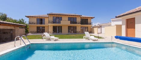 A two-story building with a swimming pool and lounge chairs.